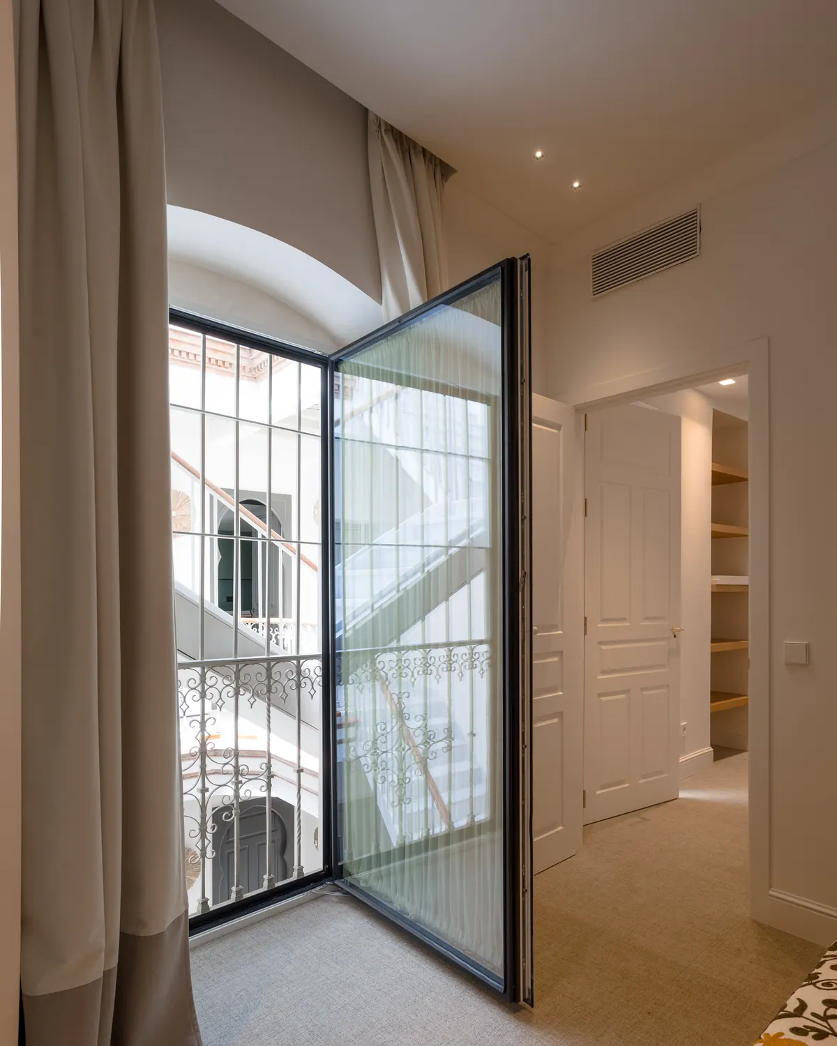 Puerta de aluminio negro acristalada abierta hacia el patio de un edificio histórico