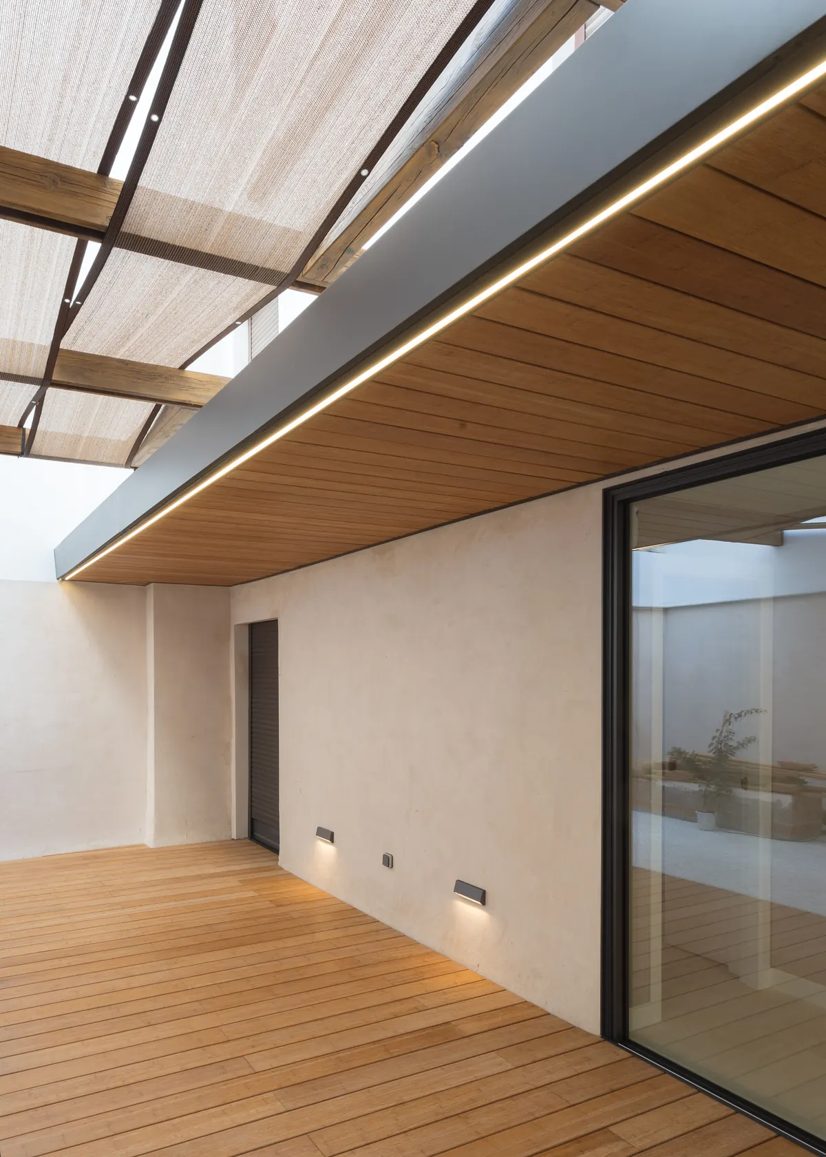 Patio con tarima Grad, techo de madera con perfil de luz y gran ventanal de aluminio negro