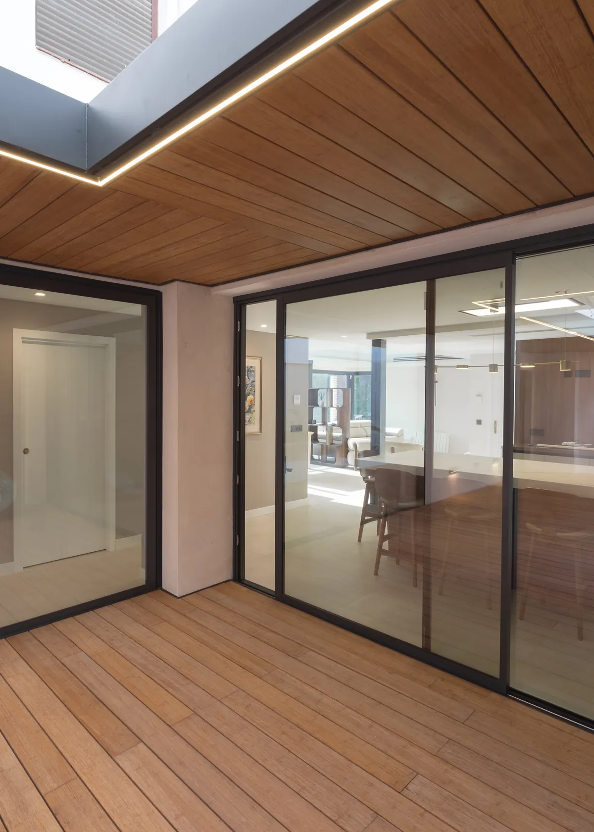 Esquina del patio con correderas de aluminio negro y techo de madera Grad iluminado