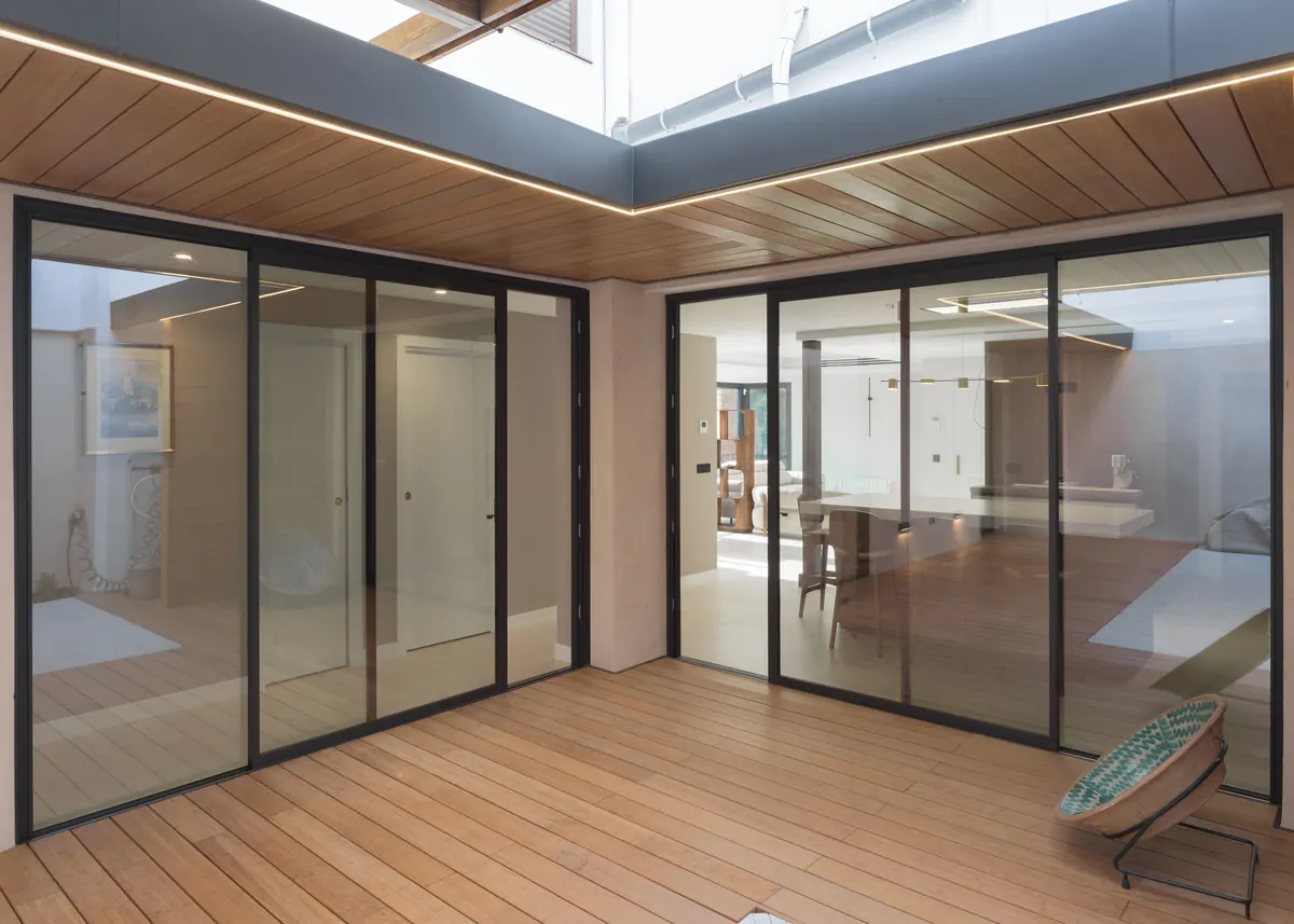 Patio en Sevilla con dos correderas de aluminio negro de suelo a techo, tarima y techo de madera Grad con luz LED