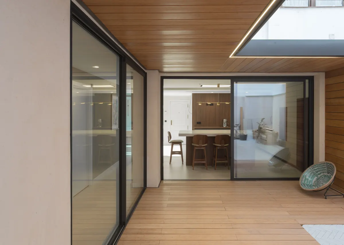 Patio exterior con correderas Strugal abiertas al comedor, suelo y techo de madera Grad