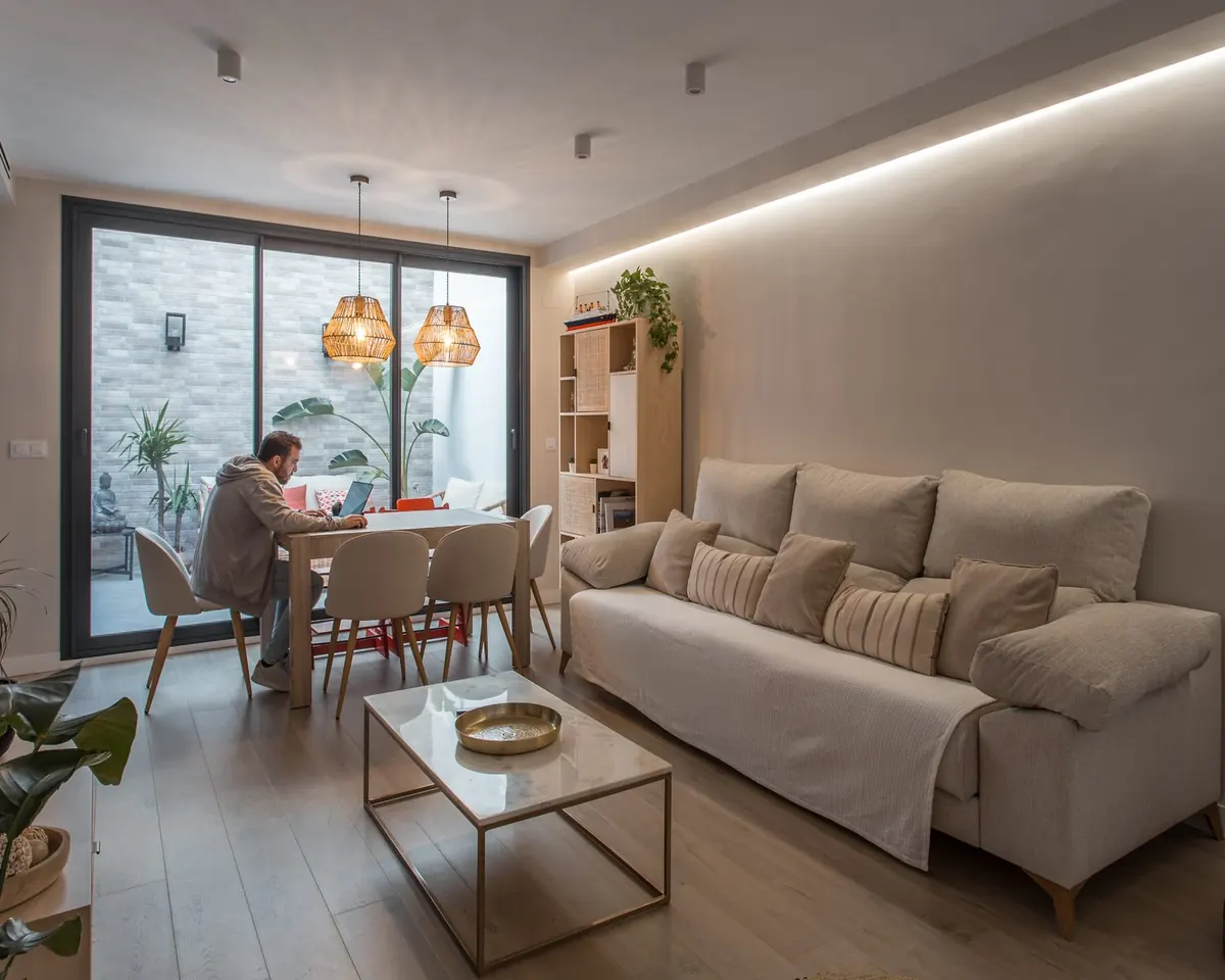 Salón con corredera de aluminio negro abierta a un patio interior, obra Palmeras Reales