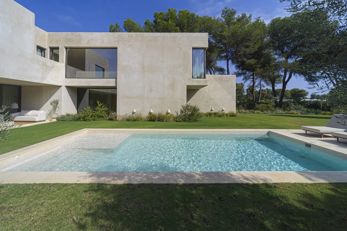 Vivienda de Sotogrande vista desde el jardín y la piscina, con grandes huecos acristalados