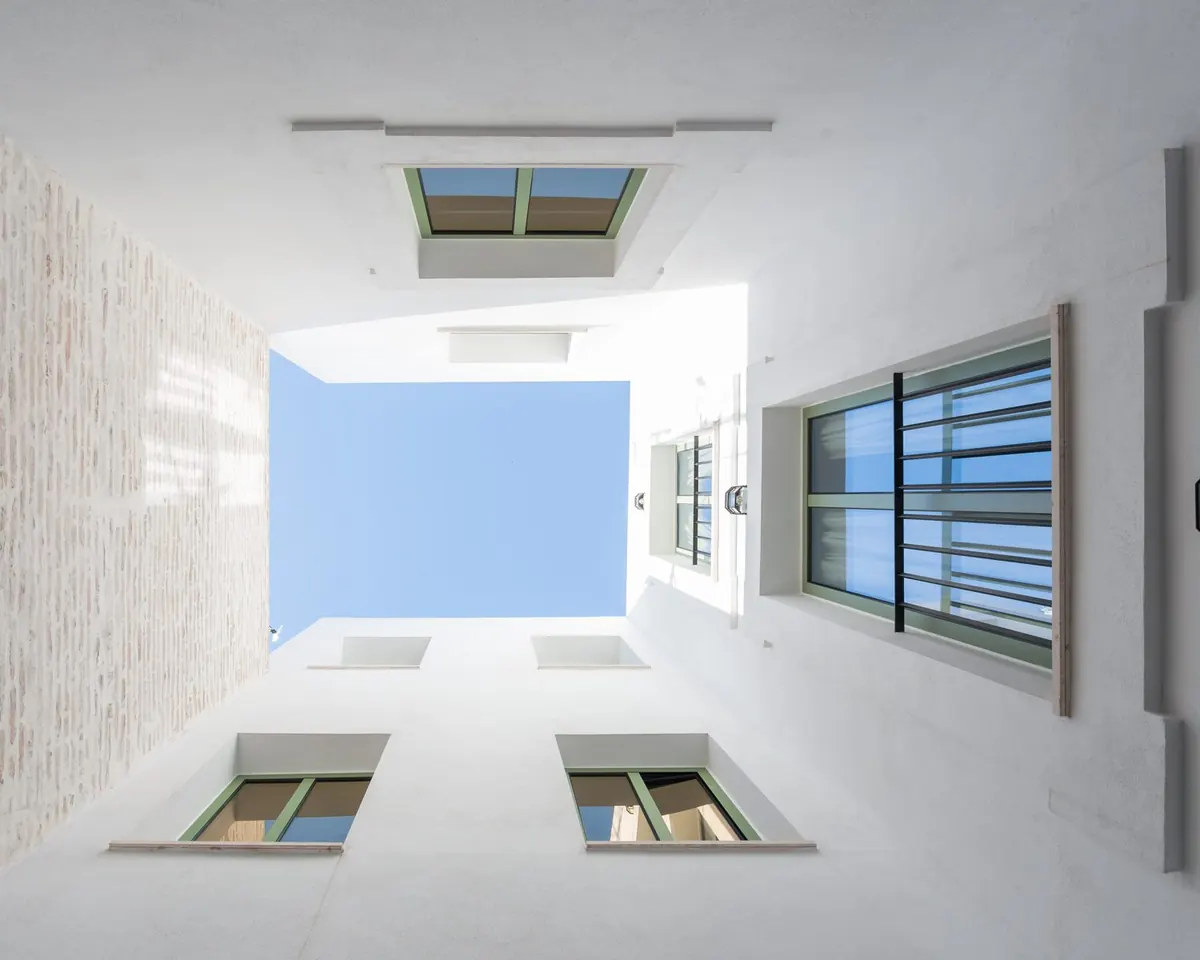 Patio interior visto desde abajo con montera acristalada y ventanas, obra Tiro de Línea