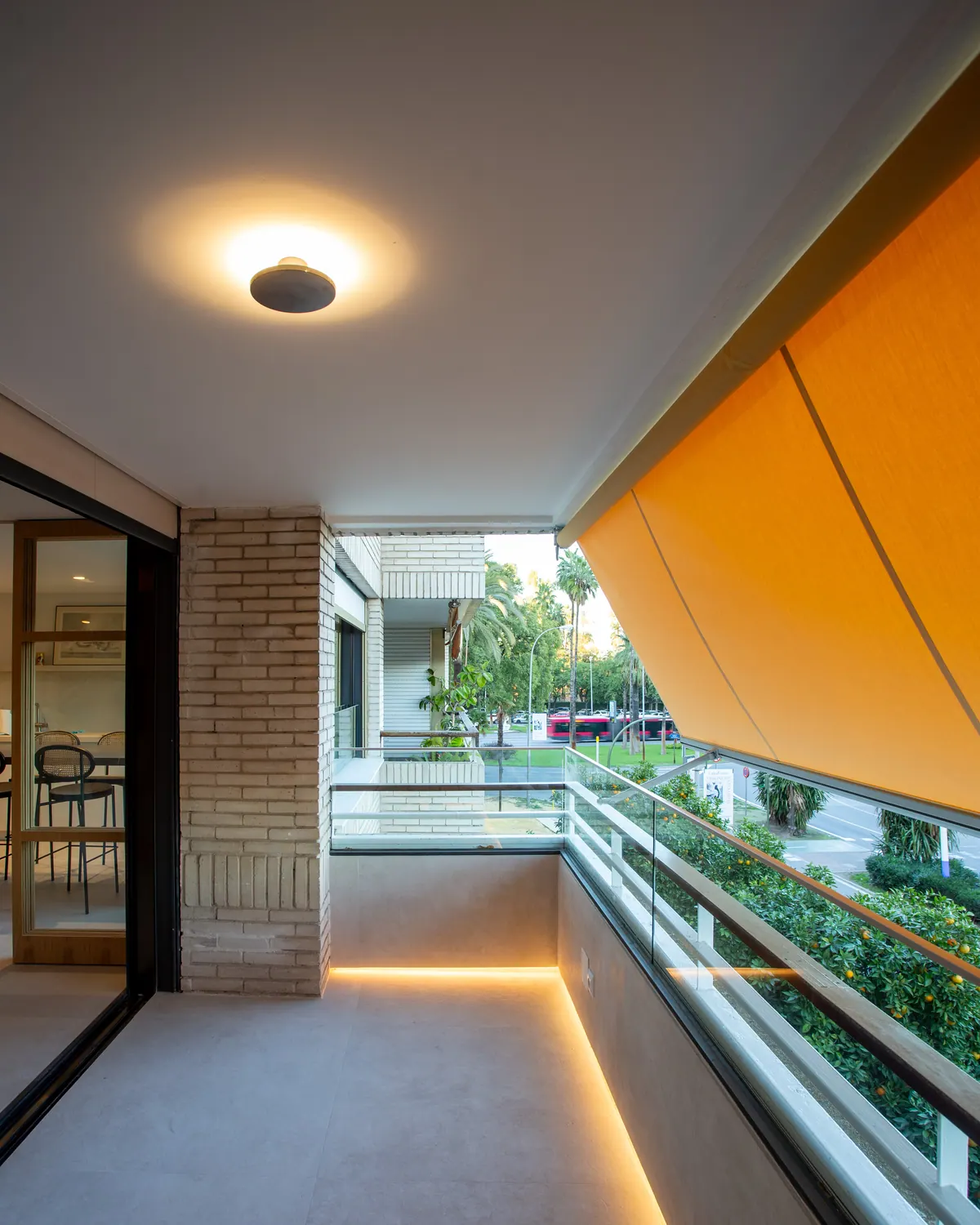 Terraza con toldo, iluminación lineal y barandilla de vidrio junto a una corredera