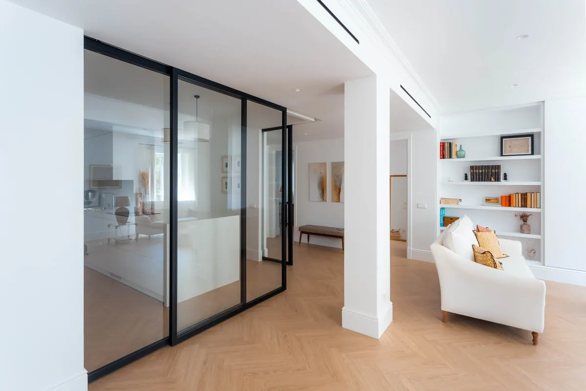Salón con puertas correderas de vidrio y perfil negro hacia la cocina